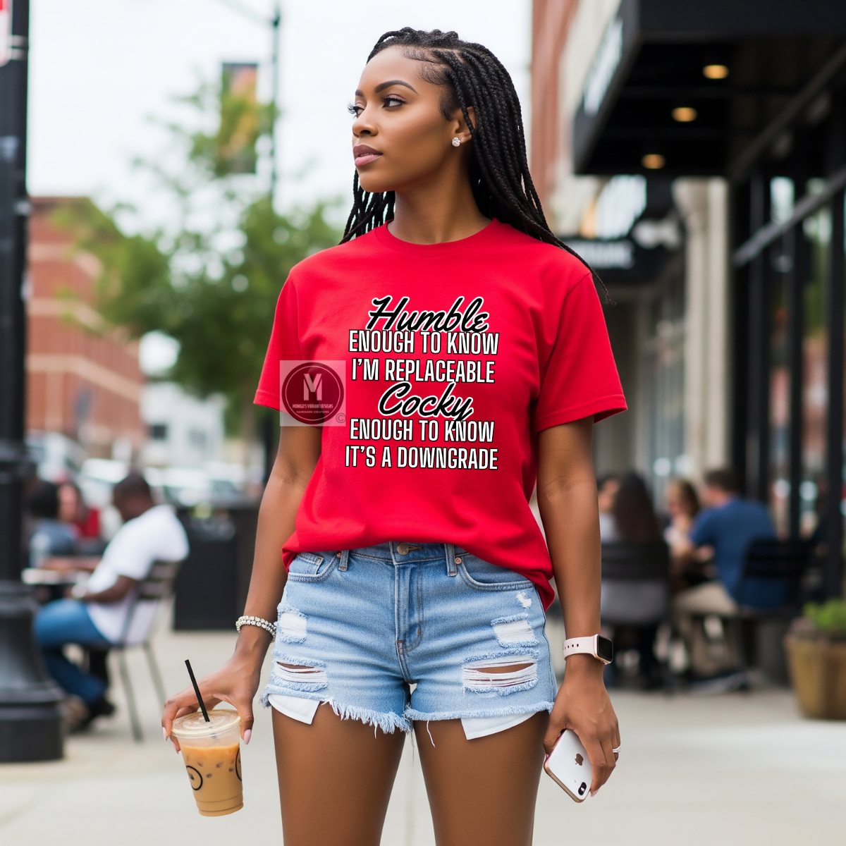 Woman wearing a red t-shirt with text, holding a drink, on a city street.