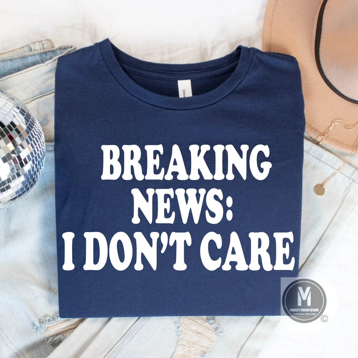 A folded navy t-shirt featuring the slogan "BREAKING NEWS: I DON'T CARE" in bold white letters, placed on a casual backdrop.