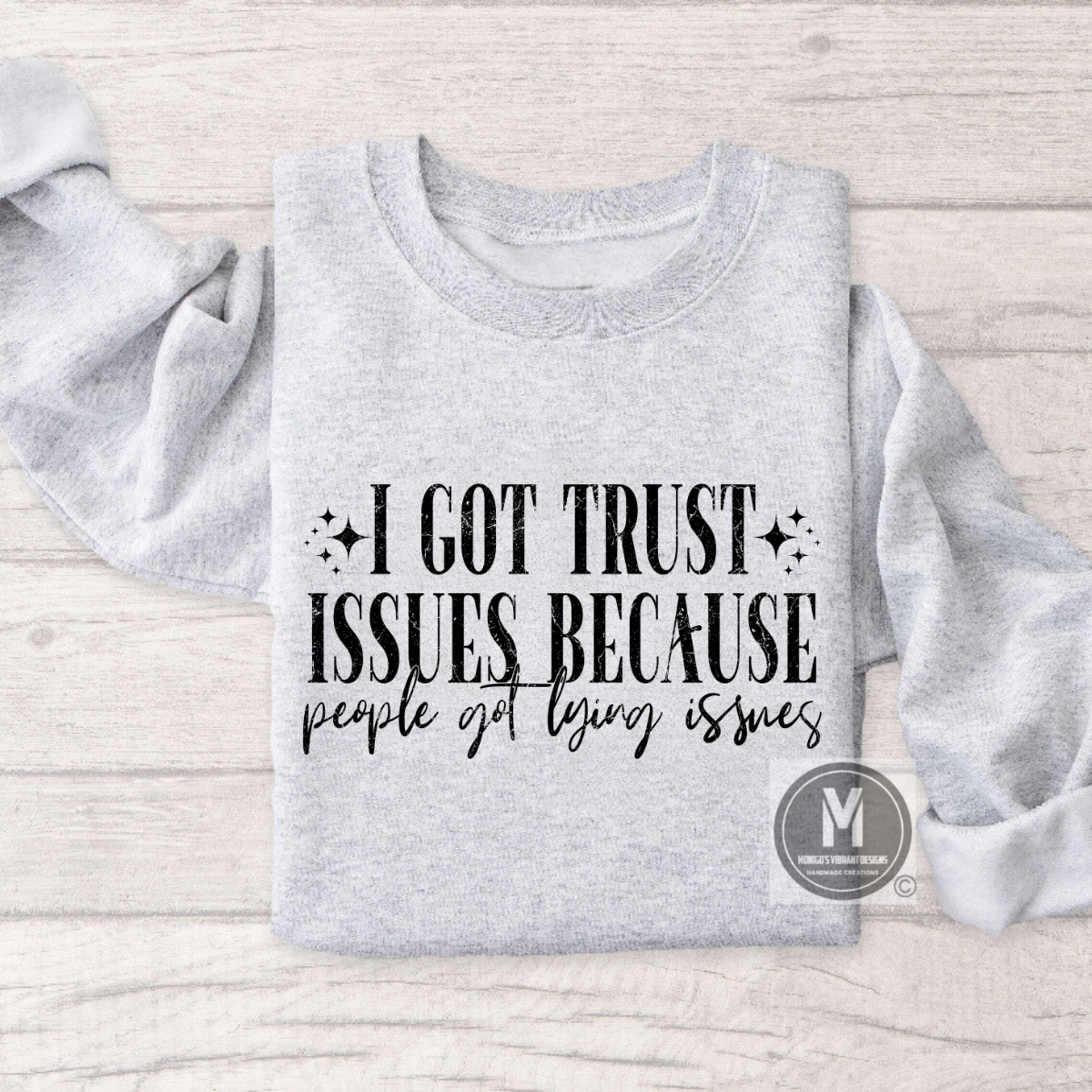 Gray sweatshirt with the text "I got trust issues because people got lying issues" in bold black letters on a wooden surface.