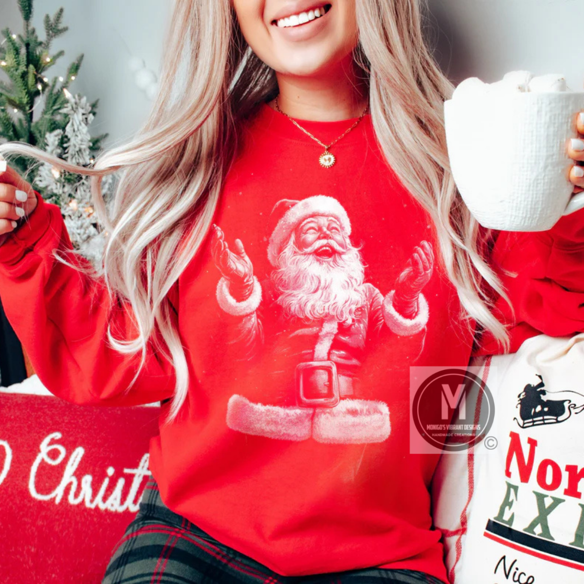 Person wearing a red sweatshirt with Santa Claus design, holding a mug and a Christmas-themed pillow.