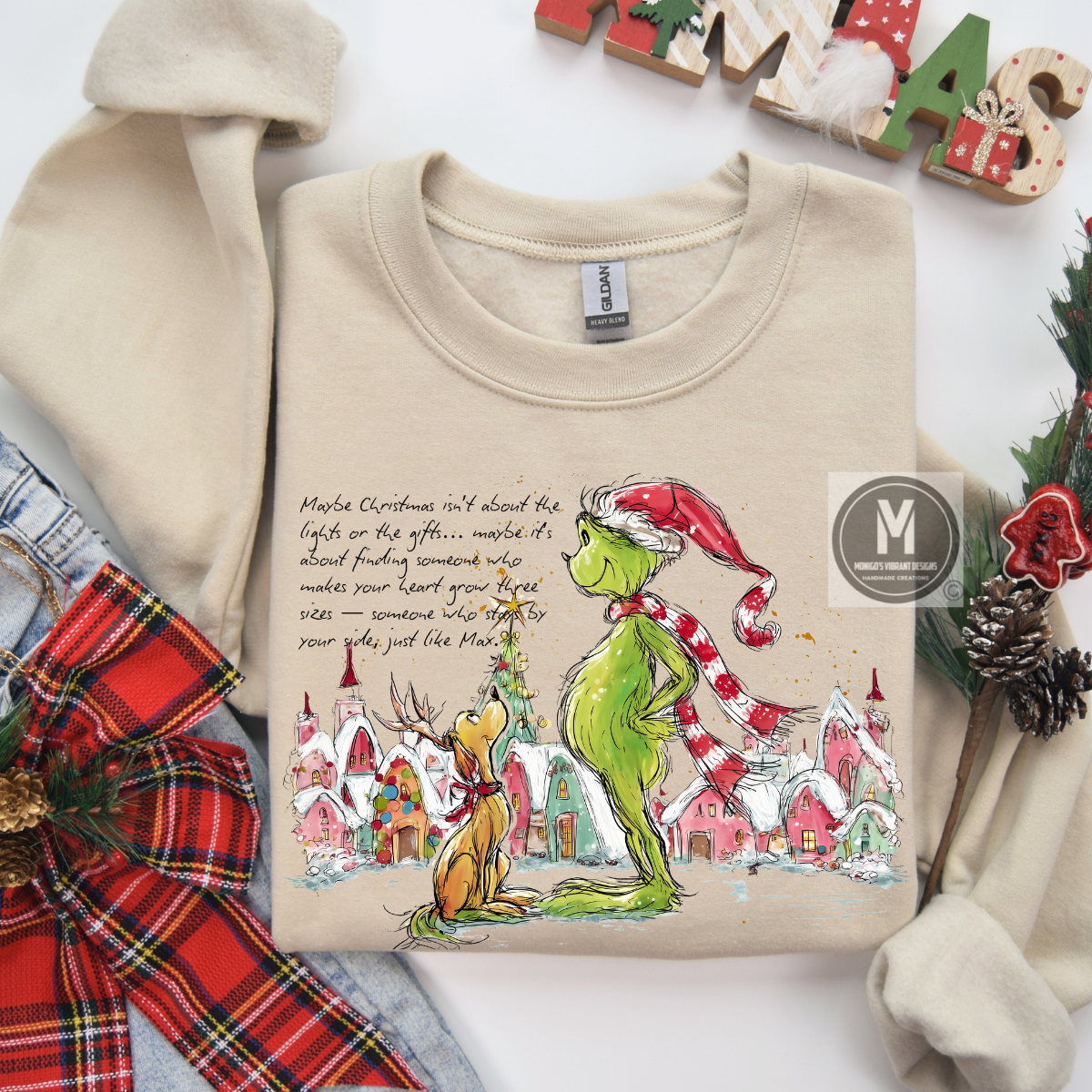 Beige sweatshirt with Grinch design and Christmas-themed text, surrounded by festive decorations.
