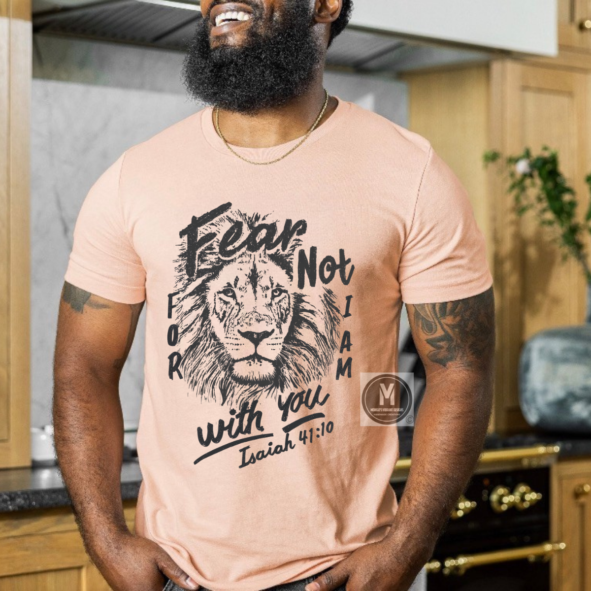 Man wearing a peach t-shirt with a lion graphic and text in a kitchen.