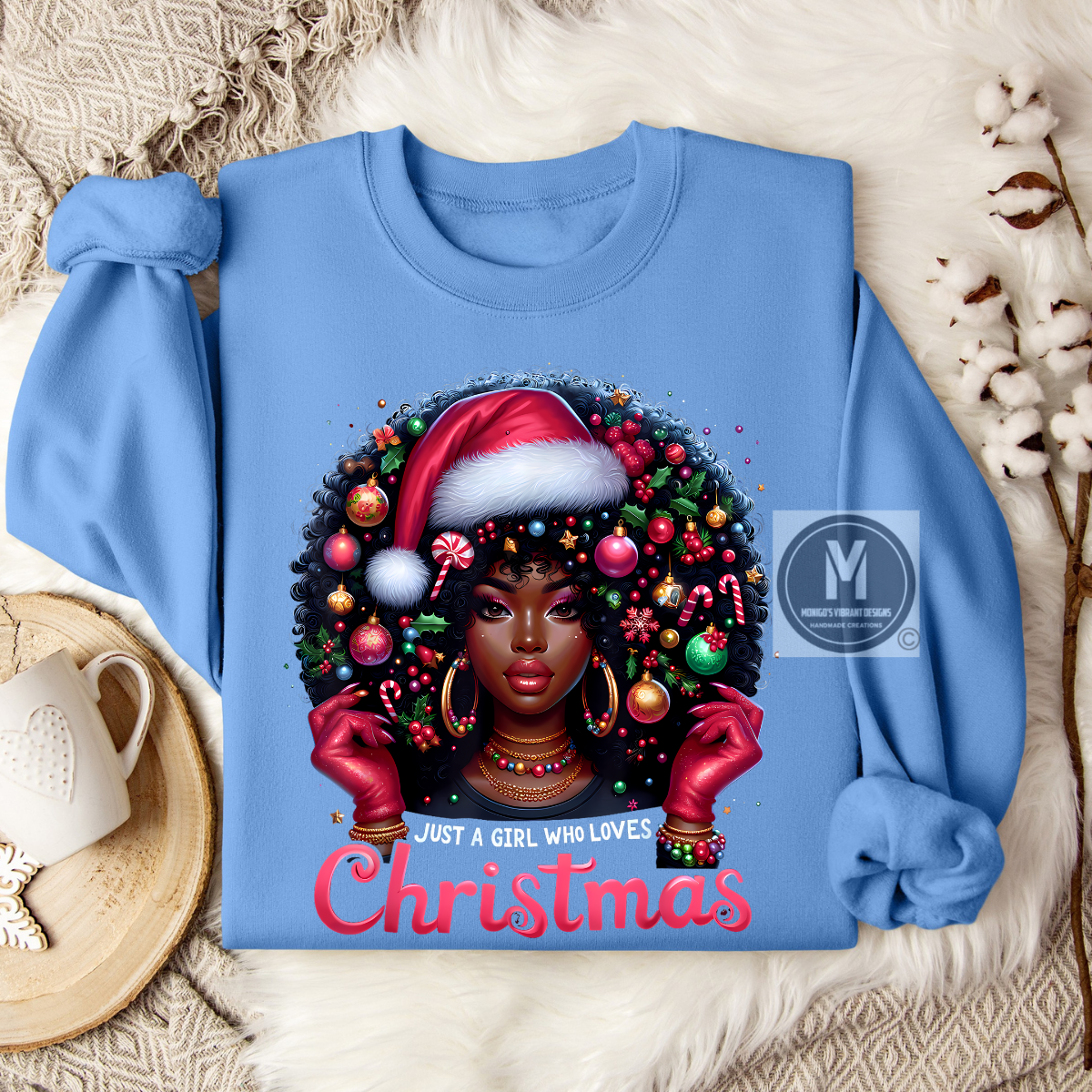 Blue sweatshirt with a festive design of a woman wearing a Santa hat and surrounded by Christmas decorations, placed on a textured surface.