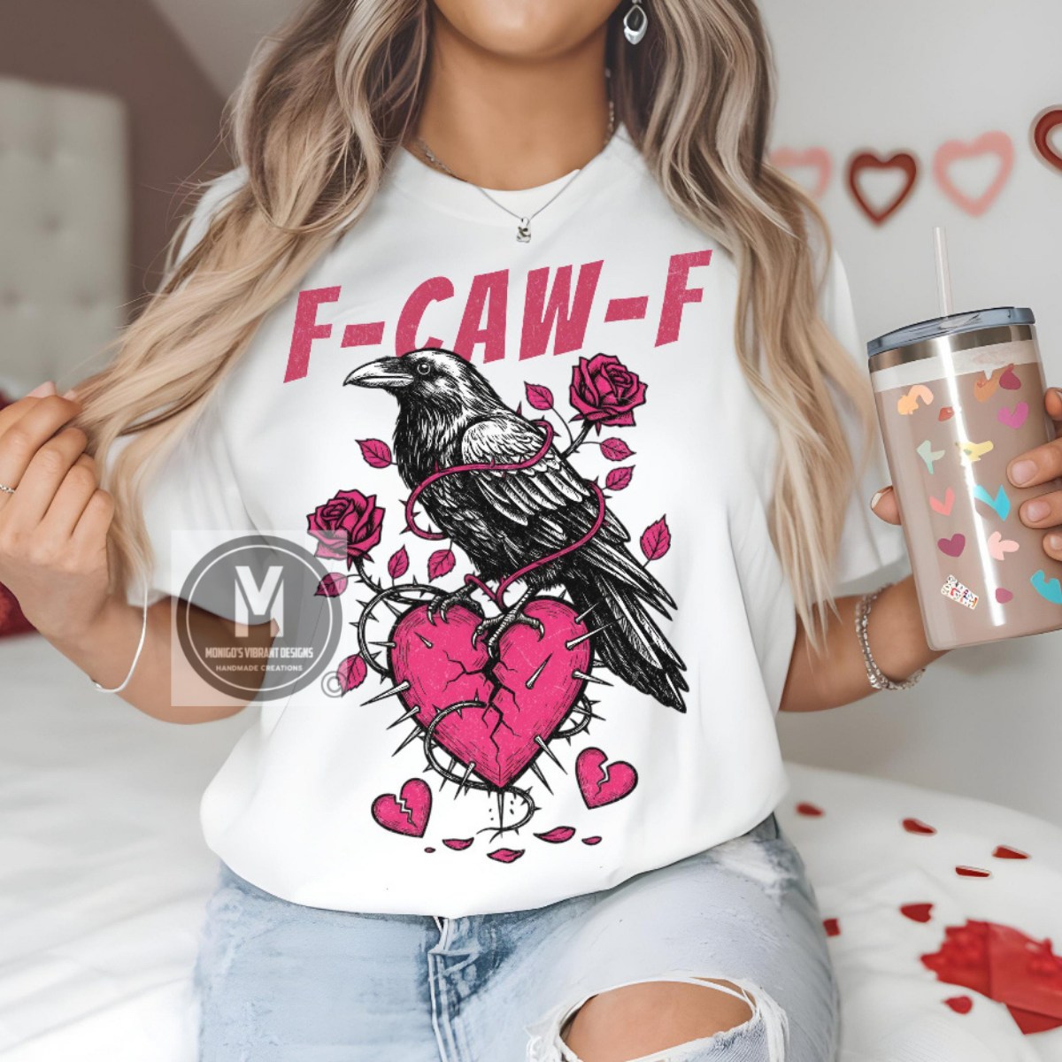Person wearing a white t-shirt with a graphic design of a crow, broken heart, and roses, holding a tumbler.