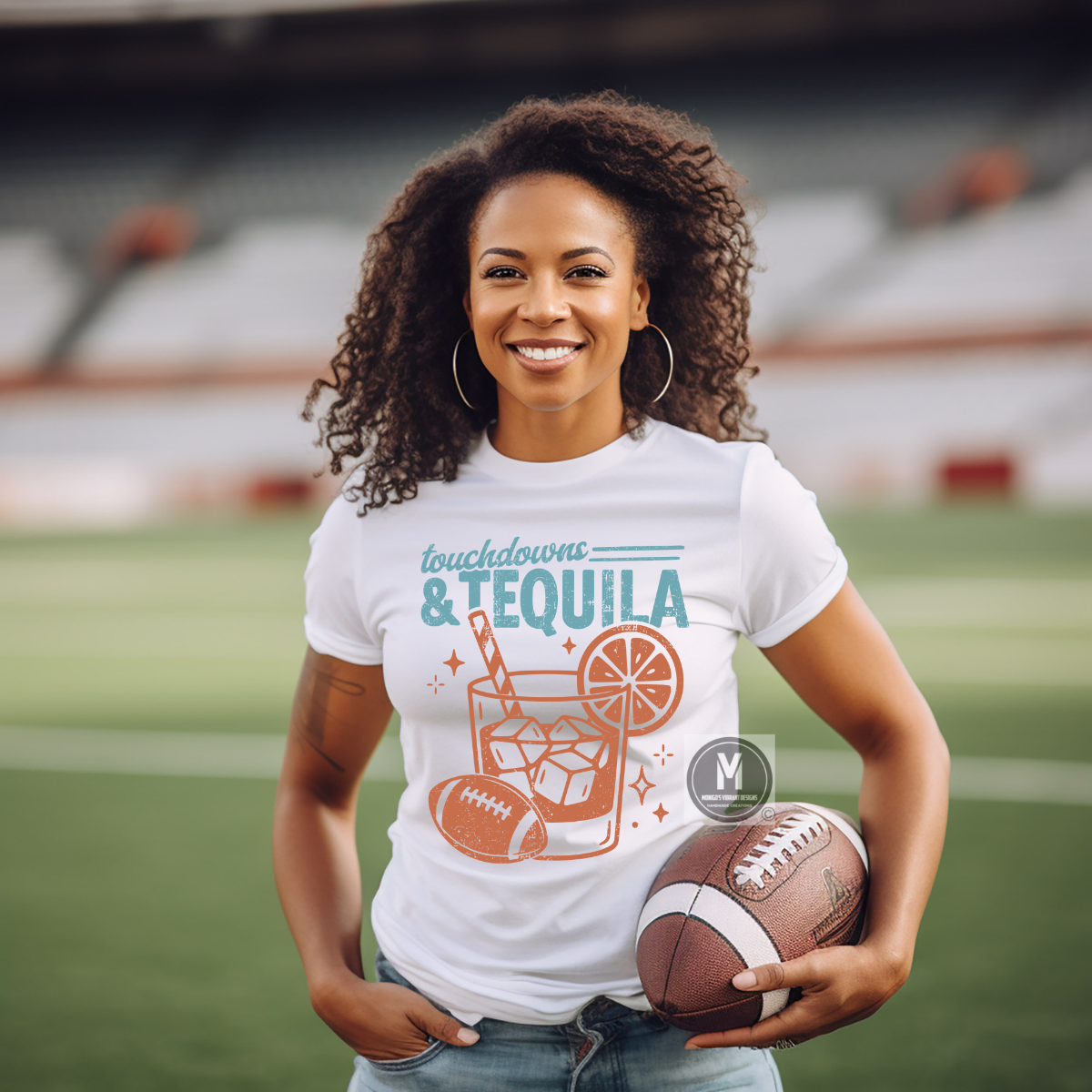 A smiling woman stands on a football field wearing a white graphic T-shirt that reads 'touchdowns & TEQUILA' with an orange and teal drink illustration, and holding a football. The background shows blurred stadium seating and the field.