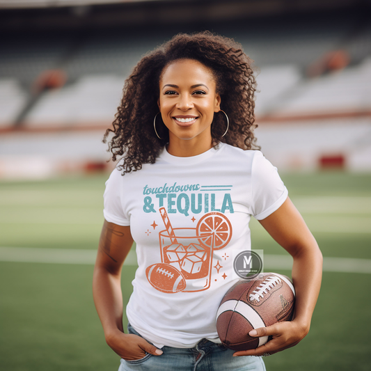 A smiling woman stands on a football field wearing a white graphic T-shirt that reads 'touchdowns & TEQUILA' with an orange and teal drink illustration, and holding a football. The background shows blurred stadium seating and the field.